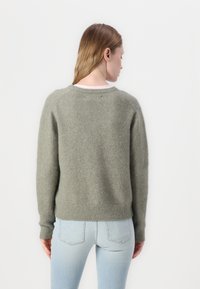 Green, textured sweater in a lightweight knit with a round neckline and ribbed cuffs, paired with light blue fitted jeans.