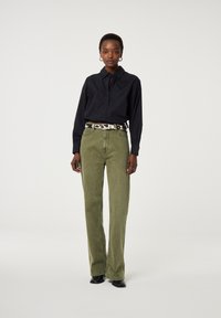 Zwarte button-up shirt met een hartdetail, gecombineerd met olijfgroene wijde jeans en een gestreepte riem. Zwarte laarzen maken de outfit compleet.