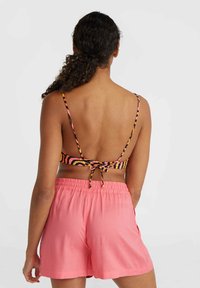 Braided back bikini top with multicolored animal print, paired with loose-fitting, pink shorts featuring an elastic waistband.