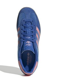 Μπλε σουέτ αθλητικά παπούτσια με ροζ τρεις ρίγες, υφή στην γλώσσα και λογότυπο. Διαθέτουν στρογγυλή μύτη και λαβή από βερύκοκο.