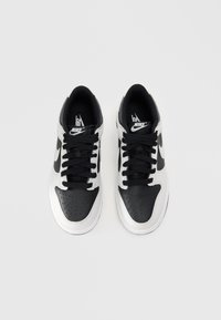 Črno-beli Nike športni čevlji z gladkim usnjenim zgornjim delom, perforirano območje prstov, črnimi vezalkami in logotipom na ježku.