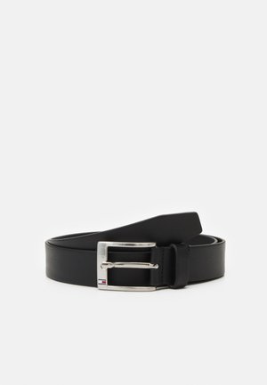 Zwarte leren riem met zilverkleurige rechthoekige gesp en een kleine rood, wit en blauw detail op de gesp, opgerold gelegd op een witte achtergrond.