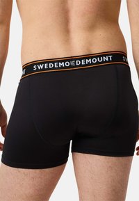 Czarne elastyczne bokserki ze zwartym pasem w kolorze czarnym z białymi i pomarańczowymi napisami, zaprojektowane dla wygody i dopasowania.