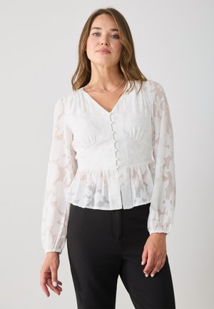 Wit peplum blouse met doorschijnende, gemusterde lange mouwen, v-hals en knoopsluiting in het midden. Bevat subtiele bloemenstructuur en ruches.