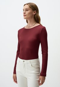 Bordeaux langermige top met een ribbelstructuur en een ronde halslijn, gecombineerd met witte slim-fit broek met een knoopsluiting.