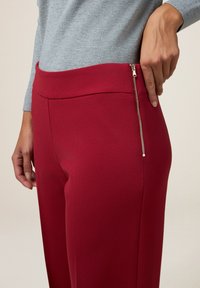 Rode op maat gemaakte broek met een gladde textuur, voorzien van een zijritszak en een brede tailleband, gecombineerd met een lichtgrijze geribde top.