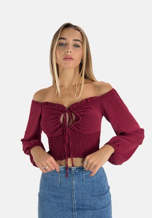 Haut bordeaux décolleté avec un design froncé et une fermeture à nouer. Manches longues avec des poignets élastiques. Tissu doux, silhouette ajustée.