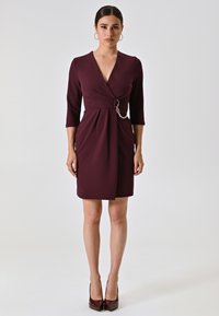 Burgunderfarbene Wickelkleid mit Dreiviertelärmeln, V-Ausschnitt und einem Gürtel, der durch eine Kettenakzent geschlungen ist. Glattes Material, knielanges Design.