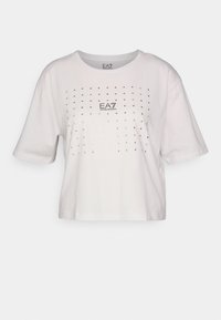 Bílý bavlněný tričko s cropped střihem, kulatým výstřihem, krátkými rukávy a kovovými nýty uspořádanými do mřížkového vzoru.