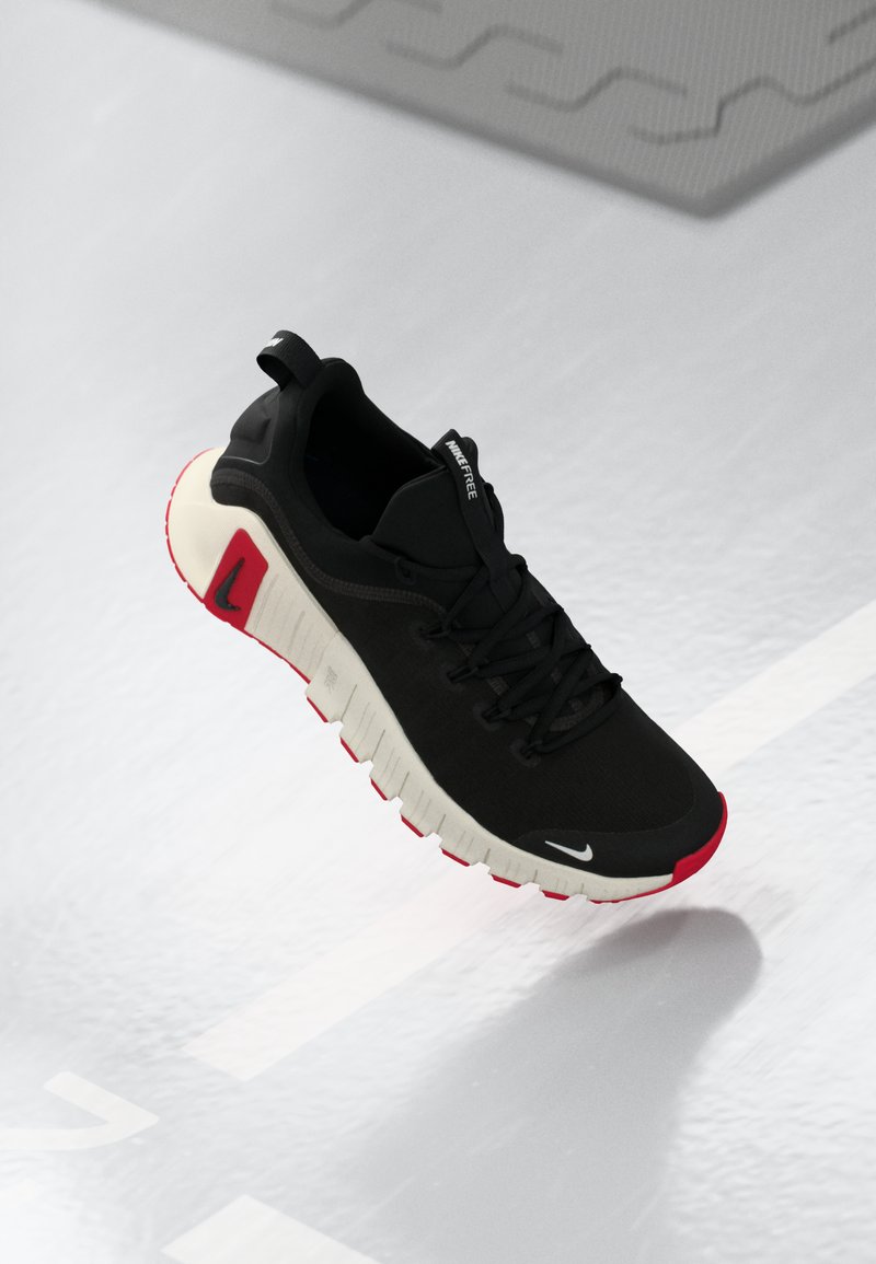 Sort-hvid Nike løbesko med røde detaljer, svævende over en lysegrå tekstureret overflade med hvide linjer og former.