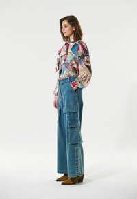 Blusa de seda floral con detalles de volantes en colores pastel, combinada con unos pantalones cargo de pierna ancha en azul claro que cuentan con múltiples bolsillos y puños.