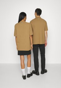 Ruske oversized polo majice s kratkim rukavima, koje nose dvije figure okrenute leđima jedna drugoj, s malim logom na kragnu.