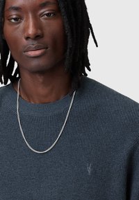 Maglione a coste blu scuro con scollo a girocollo, caratterizzato da un delicato logo ricamato e una collana in argento.