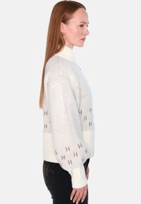 L�øs strikkegenser i kremfarge med ribbestrikkede mansjetter og krage. Har et subtilt "H" mønster i lys brun. Myk tekstur, oversized passform.