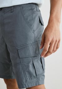 Szürke cargo nadrág, sima textúrájú anyagból, oldalsó zsebekkel, övtartókkal és varrt részletekkel.