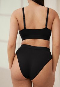 Zwarte bralette en high-waisted panties van gladde stof, met verstelbare bandjes en een naadloos ontwerp voor comfort.