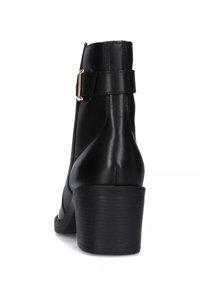 Stivale alla caviglia in pelle nera con tacco sagomato, dettaglio in fibbia dorata e texture liscia. La parte posteriore presenta una silhouette elegante e una cucitura ben definita.