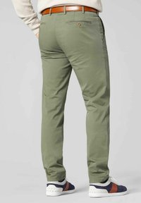 Grüne Baumwollhosen mit schmaler Passform, Gesäßtaschen und einem braunen Ledergürtel, kombiniert mit weißen und marineblauen Sneakers.