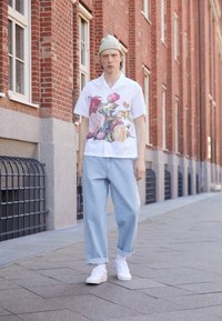 Camicia bianca a maniche corte con stampa floreale vivace; pantaloni in denim a gamba larga color blu chiaro; sneakers bianche; berretto leggero.