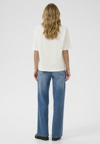 Top bianco a maniche corte con vestibilità morbida, abbinato a jeans a gamba larga blu chiaro. Stivali neri robusti completano l'outfit.