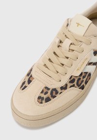 Sneaker in suede beige con pannello laterale in stampa leopardata, punta rotonda e lacci beige. Presenta un piccolo tag con logo dorato vicino alla linguetta.