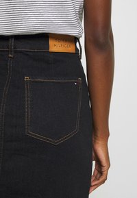Gonna di jeans di colore blu scuro con cuciture arancioni, caratterizzata da un'etichetta in pelle marrone sul retro e una tasca posteriore singola con un piccolo dettaglio del logo.