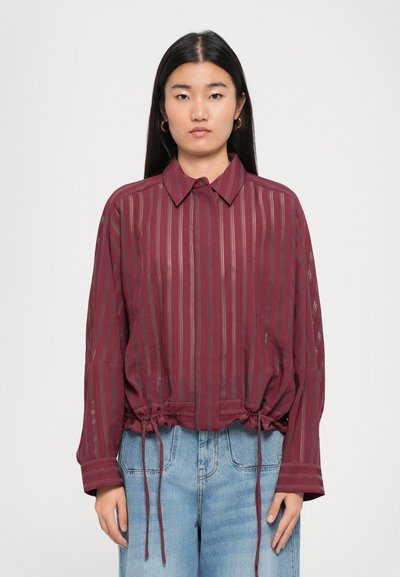 Blusa a strisce bordeaux con colletto, vita arricciata e dettagli con cordoncino. Maniche lunghe con dettagli a trama aperta.