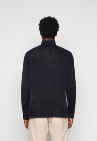 Svart, texturerad tröja med hög krage och långa ärmar, med en avslappnad passform och ett mjukt, fluffigt material.