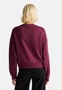 Sudadera burdeos con un corte relajado, puños y dobladillo acanalados, y cuello redondo. Hecha de un tejido suave y texturizado. Combinada con pantalones negros.