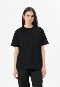 T-shirt en coton noir à manches courtes, col rond et logo ton sur ton subtil sur la poitrine gauche. Porté avec un pantalon noir.