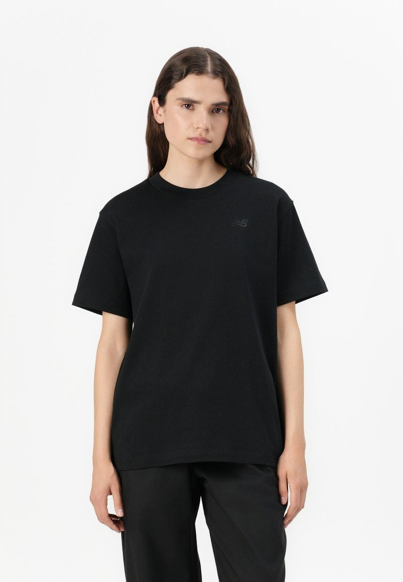 T-shirt en coton noir à manches courtes, col rond et logo ton sur ton subtil sur la poitrine gauche. Porté avec un pantalon noir.