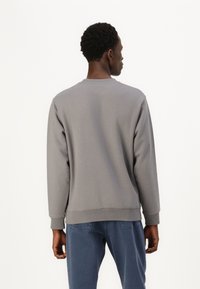 Grauer Sweatshirt mit Rundhalsausschnitt, langen Ärmeln, gerippten Bündchen und Saum, kombiniert mit blauen Hosen. Glatte Stoffoberfläche, minimalistisches Design.