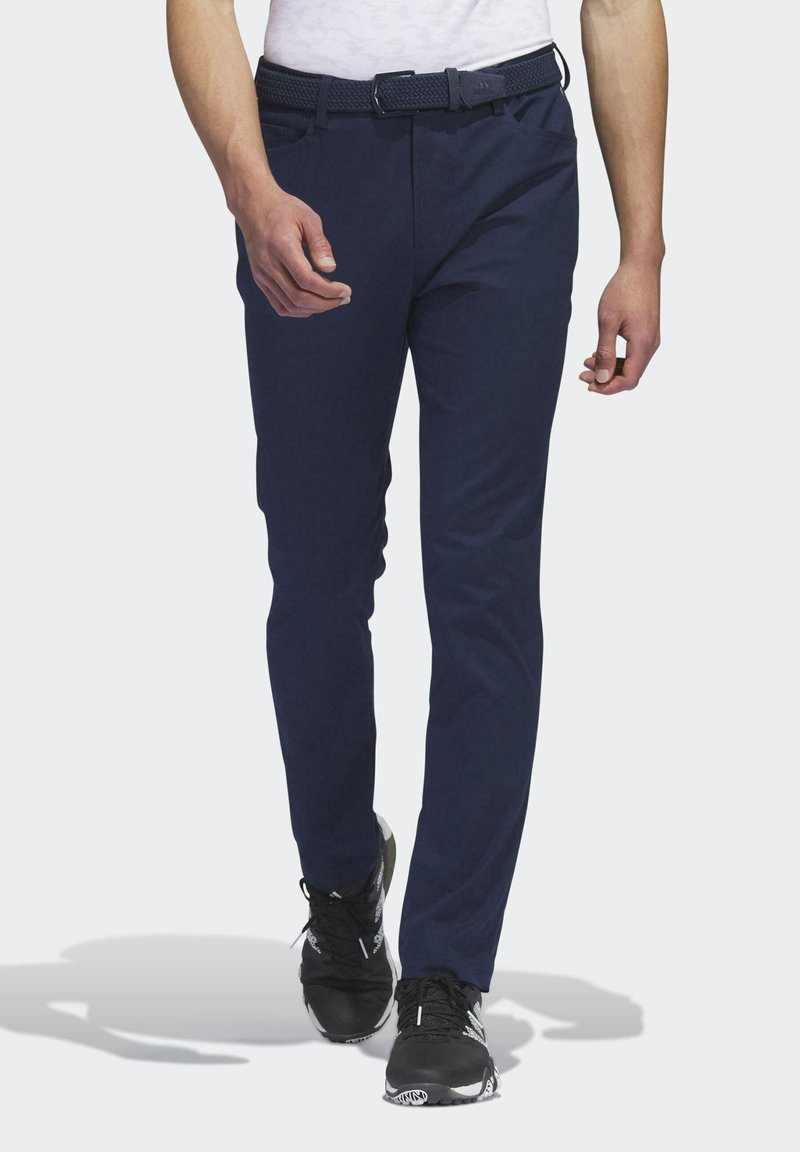 Navyblauwe, slimfit broek gemaakt van een gladde stof, met een geweven riem en standaardzakken, gecombineerd met zwarte sportschoenen.