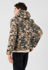 Camouflage donzen jas met een capuchon, met een mix van groene, bruine en beige kleuren, doorgestikte structuur en geribbelde manchetten.