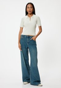 Lichtgroene geribde poloshirt met korte mouwen, gecombineerd met blauwe wijde jeans. De outfit heeft een casual pasvorm en minimale details.