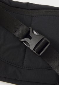 Black nylon bag detail featuring a textured buckle closure and adjustable strap. Visible stitching on the fabric adds visual interest.
