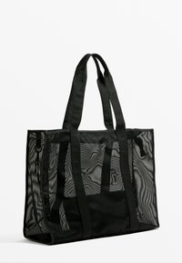 Black mesh tote bag with dual sturdy straps, rectangular shape, open design for visibility, and textured surface detail.