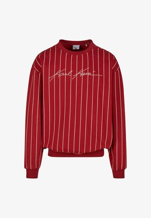 Raudonas džemperis su kreminiais vertikaliais dryžiais, apvaliu iškirpimu ir elastinėmis rankovėmis. Priekyje yra išlenktas prekės ženklas. Pagamintas iš minkštos medžiagos.