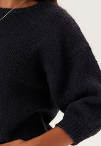 Mörkblå stickad tröja med en texturerad yta, vida ärmar och en avslappnad passform, med rundad halsringning och mjukt material.