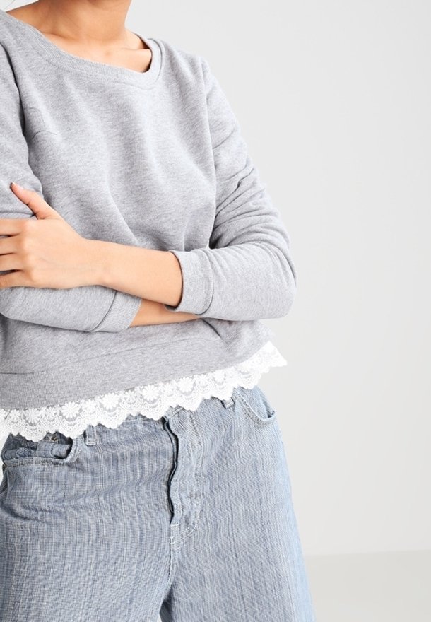 Ljusgrå sweatshirt med vit spetskant i nederkant, som har en avslappnad passform och långa ärmar. I kombination med ljusblå denimjeans.