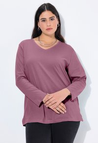 Lange mouwen, V-hals top in lavendelkleurige stof met een relaxte pasvorm. Heeft een rechte zoom en subtiele textuur. Gecombineerd met donkere jeans.