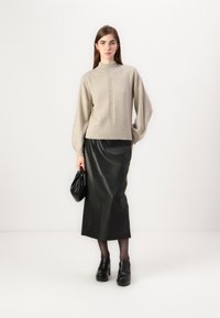 Beige stickad tröja med hög krage och ribbat mönster, kombinerad med en slank svart läderkjol, svarta platåskor och en svart väska.