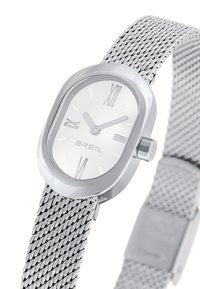 Montre avec bracelet en maille argentée, boîtier ovale, cadran blanc, chiffres romains et couronne sur le côté. Dispose d'une finition métal poli et d'un design épuré.