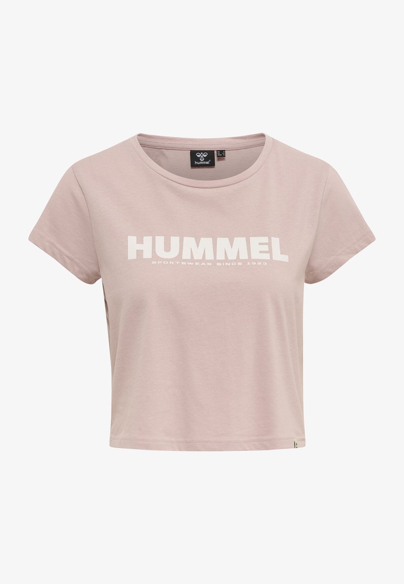 Světle růžový crop top vyrobený z měkké bavlny s kulatým výstřihem. Má výrazný bílý text "HUMMEL" a pod ním nápis "SPORTSWEAR SINCE 1923".