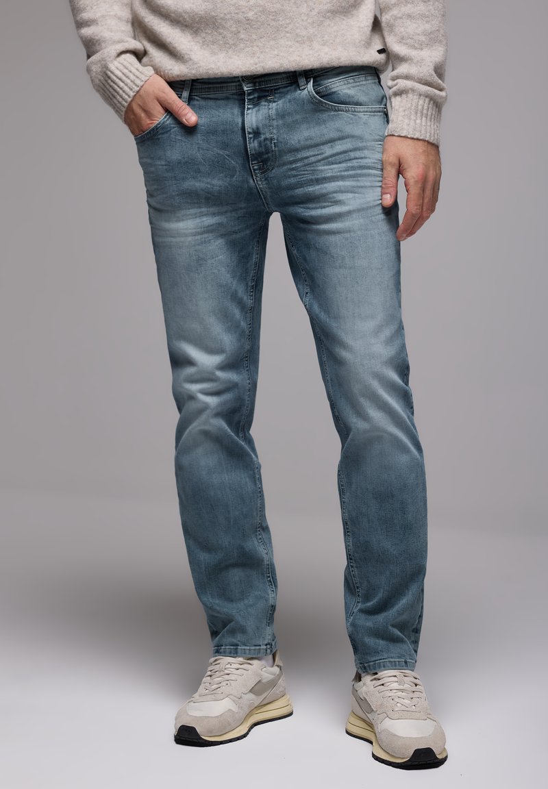 Jeans in denim blu chiaro con una vestibilità rilassata, caratterizzati da leggere sfumature e design a cinque tasche, abbinati a sneakers color crema.