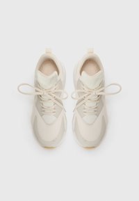 Lys beige treningssko med mesh-overdel, glatte aksenter, flate lisser og en teksturert såle. Har en løkke ved hælen for enkel påføring.