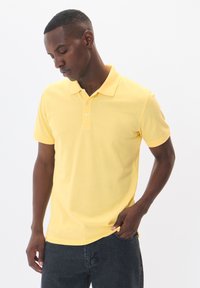 Gul polo skjorta gjord av bomull, med standardkrage, korta ärmar, treknapplet och en slät yta.