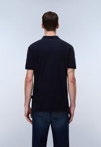 Marineblå polo-shirt med korte ærmer, blødt bomuldsmateriale, klassisk krave og lille logodetalje på bagsiden af halsen, kombineret med blå denimbukser.