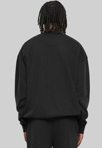 Svart oversized sweatshirt med rund halsringning, långa ärmar och ribbade mudd. Den är tillverkad av mjukt material, har en enkel design och inga synliga logotyper.