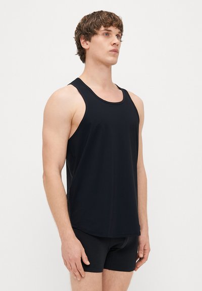 Črna brezrokavna majica iz mehkega materiala, z okroglim izrezom in sproščenim krojem, v kombinaciji s črnimi kratkimi hlačami.